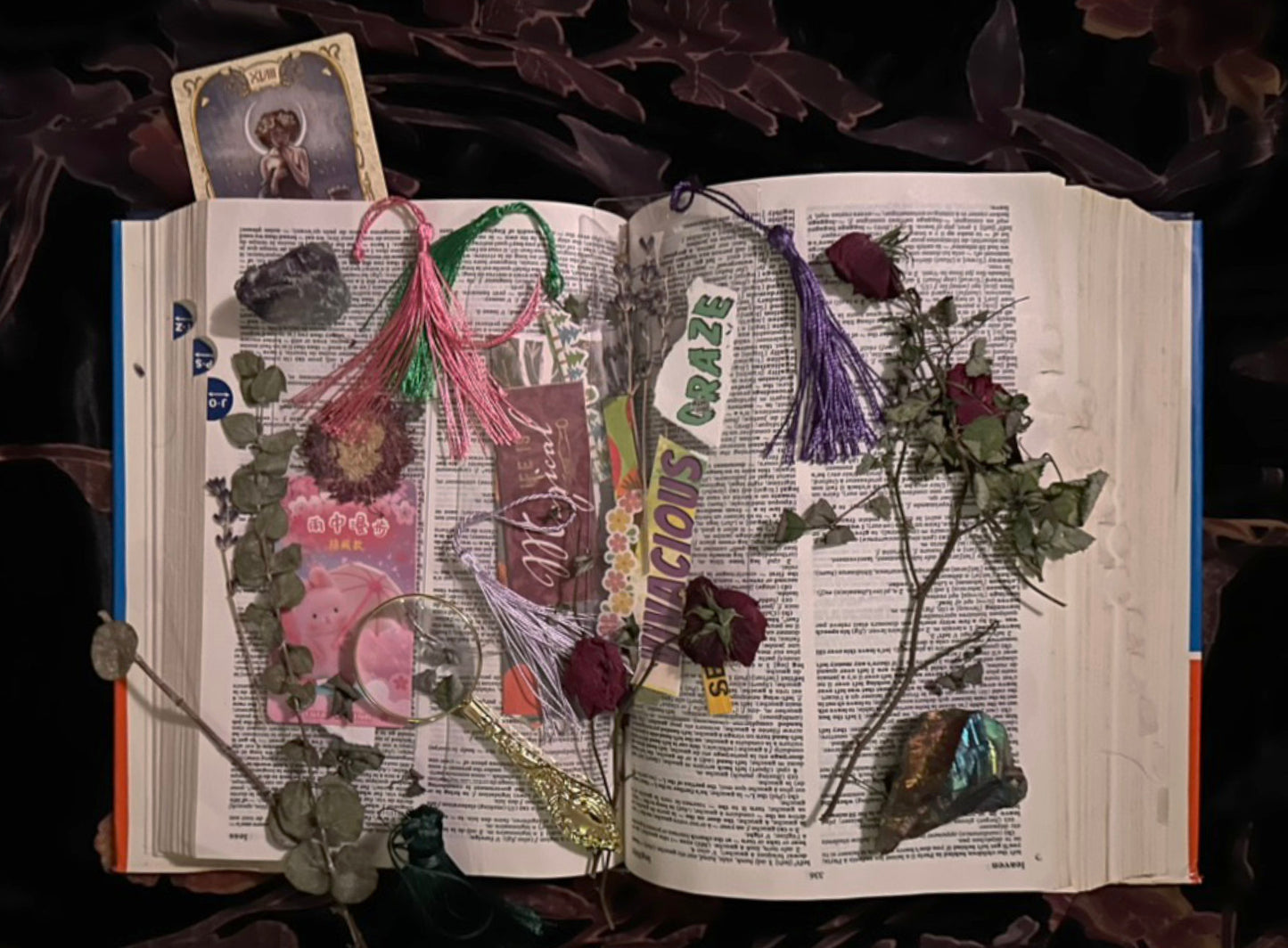 Open french to english dictionary with decorative elements like flowers, tassels, bookmarks and a magnifying on a dark velvet floral background
